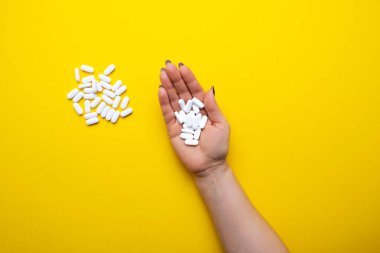 Sarı arka planda beyaz haplı kadın eli..