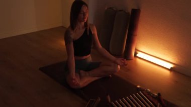 Bir kadın loş, sıcak ışıkta evde yoga yapıyor..
