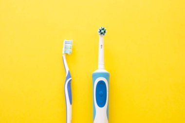 Sarı zemin üzerinde mavi renkte elektrikli ve analog diş fırçası.