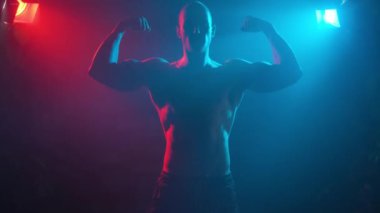 Erkek vücut geliştirici kollarındaki kasları gösteriyor. Duman içinde neon ışığı..