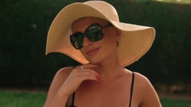 Happy girl in sunglasses, summer hat against the background of a green fence on a summer sunny day