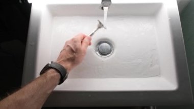 Cleaning shaving razor in bathroom sink. Rinsing off razor with water.