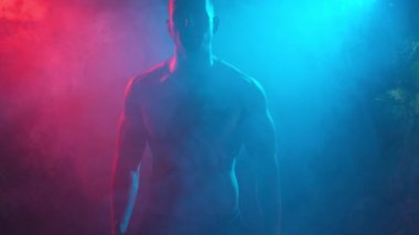 Genç kaslı bir adam renkli ışıkta dumandan çıkıyor..