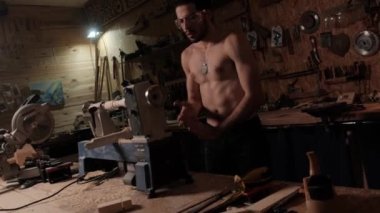 Bir marangoz torna tezgahında çalışıyor. Genç bir adam makineye ağaç dikiyor..