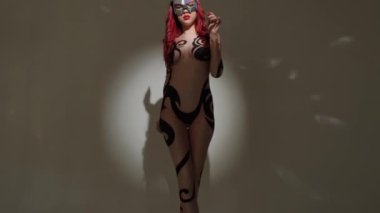 Seksi dar bir kostüm giymiş boynuzlu şeytan kız stüdyoda gri bir arka planda güzel bir şekilde dans ediyor..