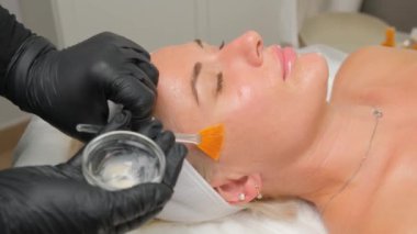 Yukarıdan gelen kozmetik uzmanı müşteriye maske takıyor, kaplıcada ya da kuaförde işlem yapıyor. Cilt bakımı, kozmetoloji ve güzellik.