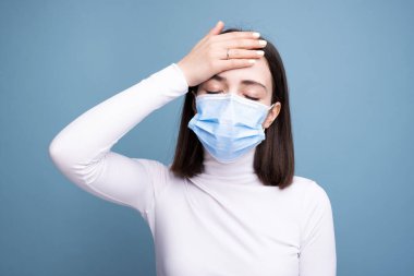Maskeli bir kız kafasını tutuyor. Sıcaklık ve baş ağrısı kavramı.