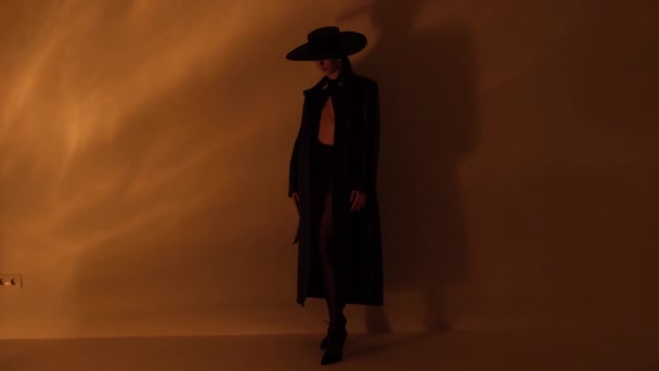 レザーコートと黒い帽子の女の子 スタジオでスタイリッシュなビデオ撮影 モデルは美しいゲートで歩きます — ストック動画