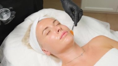 Yukarıdan gelen kozmetik uzmanı müşteriye maske takıyor, kaplıcada ya da kuaförde işlem yapıyor. Cilt bakımı, kozmetoloji ve güzellik.