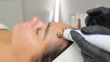 Close-up portrait of a beautiful woman with closed eyes and apparatus for skin rejuvenation. Beauty salon procedures. RF lifting. Microcurrents.