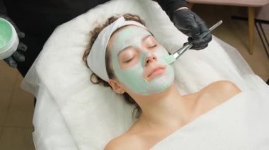 Yukarıdan gelen kozmetik uzmanı müşteriye maske takıyor, kaplıcada ya da kuaförde işlem yapıyor. Cilt bakımı, kozmetoloji ve güzellik.