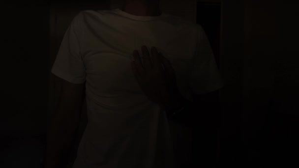 Mężczyzna Białej Koszulce Ciemnym Pokoju Trzyma Rękę Sercu Błysk Światła — Wideo stockowe