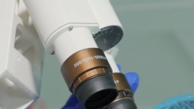 Kadın bir laboratuvar asistanı mikroskop yardımıyla maske, gözlük ve tıbbi kapak takarak virüsü inceliyor. Dikey video.