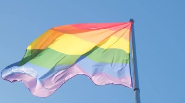 Gökkuşağı bayrağı, LGBT topluluğunun sembolü, mavi gökyüzüne karşı rüzgarda dalgalanıyor..