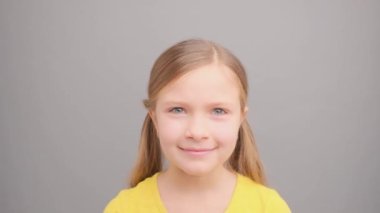 Küçük hoşnutsuz kız gri bir arka planda başını sallıyor..