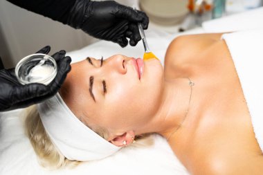 Yukarıdan gelen kozmetik uzmanı müşteriye maske takıyor, kaplıcada ya da kuaförde işlem yapıyor. Cilt bakımı, kozmetoloji ve güzellik.