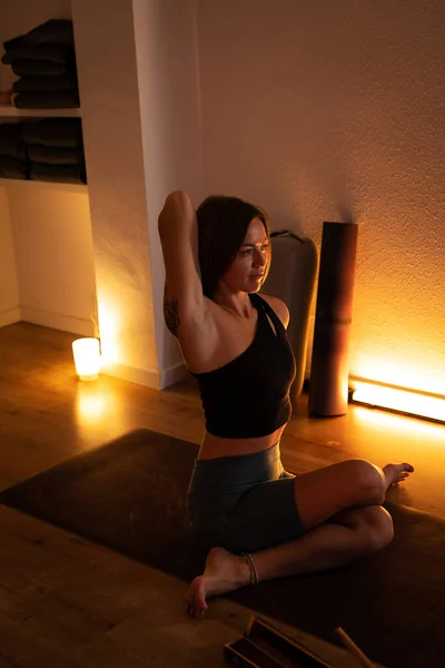 A woman practices yoga in a dark room and warm light.