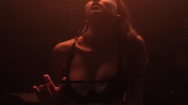 İç çamaşırlı güzel bir kız karanlık bir odada sıcak bir ışıkla duş alıyor..