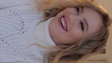 Sıcak bir süveter ve bir fincan çay giymiş güzel bir sarışın, yakın plan bir portre. Dikey video.