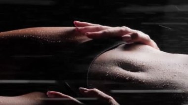 Siyah arka planda, duşta iç çamaşırlarıyla güzel bir vücudu olan bir kız. Dikey video.