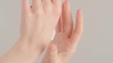 Kremalı güzel genç kadın elleri. Kadın, gri arka plana krem sürüyor. Dikey video.