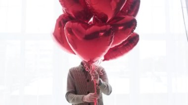 Hafif arka planda kalp şeklinde kırmızı balonları olan bir adam. Sevgililer Günü.