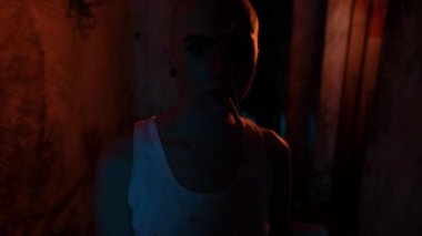 Kulaklarında tünel ve yakın çekimde sigara olan kel bir kızın portresi. Neon lambalı kasvetli oda. Kız sigara içiyor ve dumanı üflüyor..