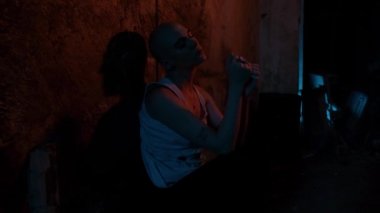 Uyuşturucu bağımlısı kel bir kadın uyuşturucu kullanmadan yoksunluk belirtileri gösterir. Neon ışıklı eski bodrum katı. Umutsuz uyuşturucu bağımlısı