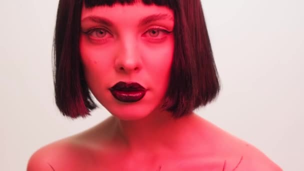 スタジオの白い背景に黒い唇とカツラを持つ赤い光の少女の肖像画 ネオンクリエイティブライトの女性 — ストック動画