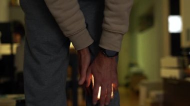 Yaralı dizini tutan pantolonlu bir adam. Acı parlak bir ışıkla parlıyor..