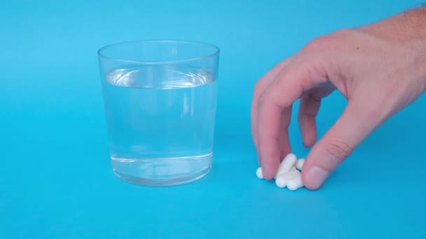 青い背景に水と丸薬が付いているガラス 白い錠剤を服用している男性のクローズアップ — ストック動画