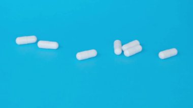 Mavi arka planda beyaz haplar. Bir erkeğin eli kapsülleri alır..