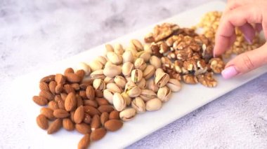 Beyaz bir tabakta farklı fındıkların karışımı. Bir kadının eli fındık alır.