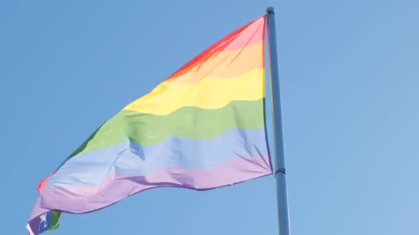Lgbtコミュニティのシンボルである虹の旗は 青い空に向かって風に揺れている — ストック動画