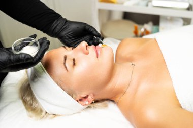 Yukarıdan gelen kozmetik uzmanı müşteriye maske takıyor, kaplıcada ya da kuaförde işlem yapıyor. Cilt bakımı, kozmetoloji ve güzellik.