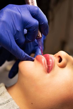 Güzellik salonunda dudaklarında kalıcı makyaj yapan genç bir kadın. Kapat.