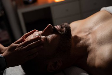 Erkek müşterisine yüz ve kafa masajı yapan profesyonel bir masözün yakın plan fotoğrafı..