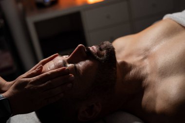 Erkek müşterisine yüz ve kafa masajı yapan profesyonel bir masözün yakın plan fotoğrafı..