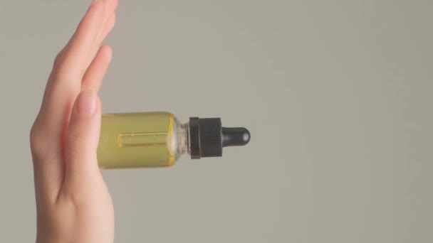 美丽的女人的手拿着化妆品油在一个透明的白色瓶子 灰色的背景 垂直录像 — 图库视频影像