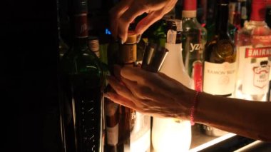 Tarragona, İspanya - 02 Ocak 2024: Kadın barmen alkol şişelerinin arka planına yakın plan çekimleri için viski dolduruyor.