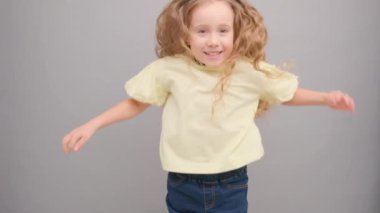 Küçük kıvırcık mutlu kız zıplar ve sevinir. Stüdyoda, gri arka planda..