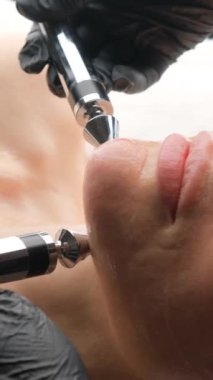 Yaşlı bir kadın mikro akım yüz gerdirme ameliyatı oluyor. Bir kozmetikçi cilt gençleştirme ve sıkılaştırmayla ilgilenir. Dikey video.