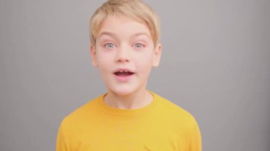 Komik çocuk. Stüdyoda sarı tişörtlü, gri arka planda bir çocuk. Şaşırdım. Küçük bir çocuk.