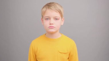 Stüdyoda 10 yaşında, gri bir arka planda sarı tişörtlü bir çocuk öfkenin nasıl hissettirdiğini gösteriyor..