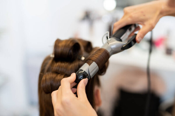 The hairdresser curls the models hair. Curling iron for curling hair close-up.