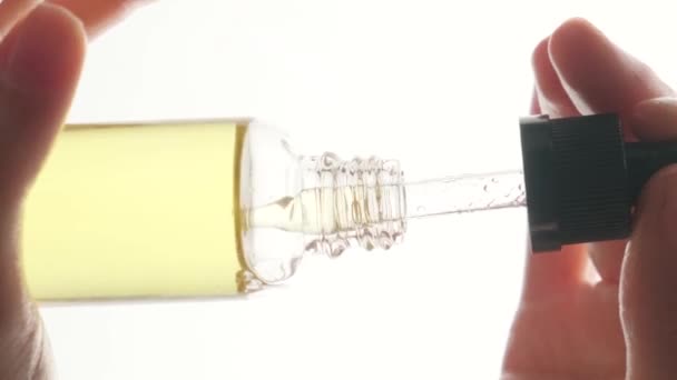 漂亮的女人的手把化妆品油放在透明的白色瓶子里 白色的背景 垂直录像 — 图库视频影像