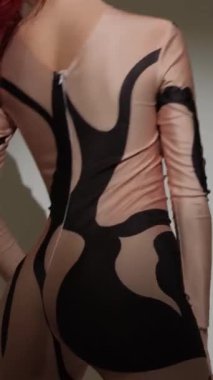 Seksi dar bir kostüm giymiş boynuzlu şeytan kız stüdyoda gri bir arka planda güzel bir şekilde dans ediyor..