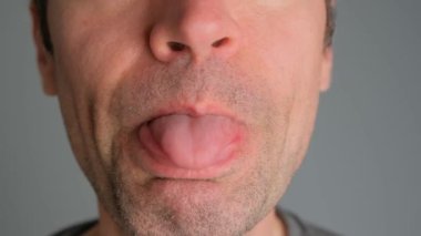 Bir adam gri arka planda dilini gösteriyor..