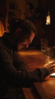 Bir gece barında genç bir adamın portresi. Bir adam kokteyl içer ve dinlenir. Dikey video.