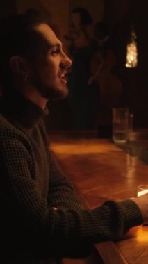 Bir gece barında genç bir adamın portresi. Bir adam kokteyl içer ve dinlenir. Dikey video.